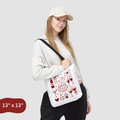 Person holding a white tote bag with red graphics on a light gray background